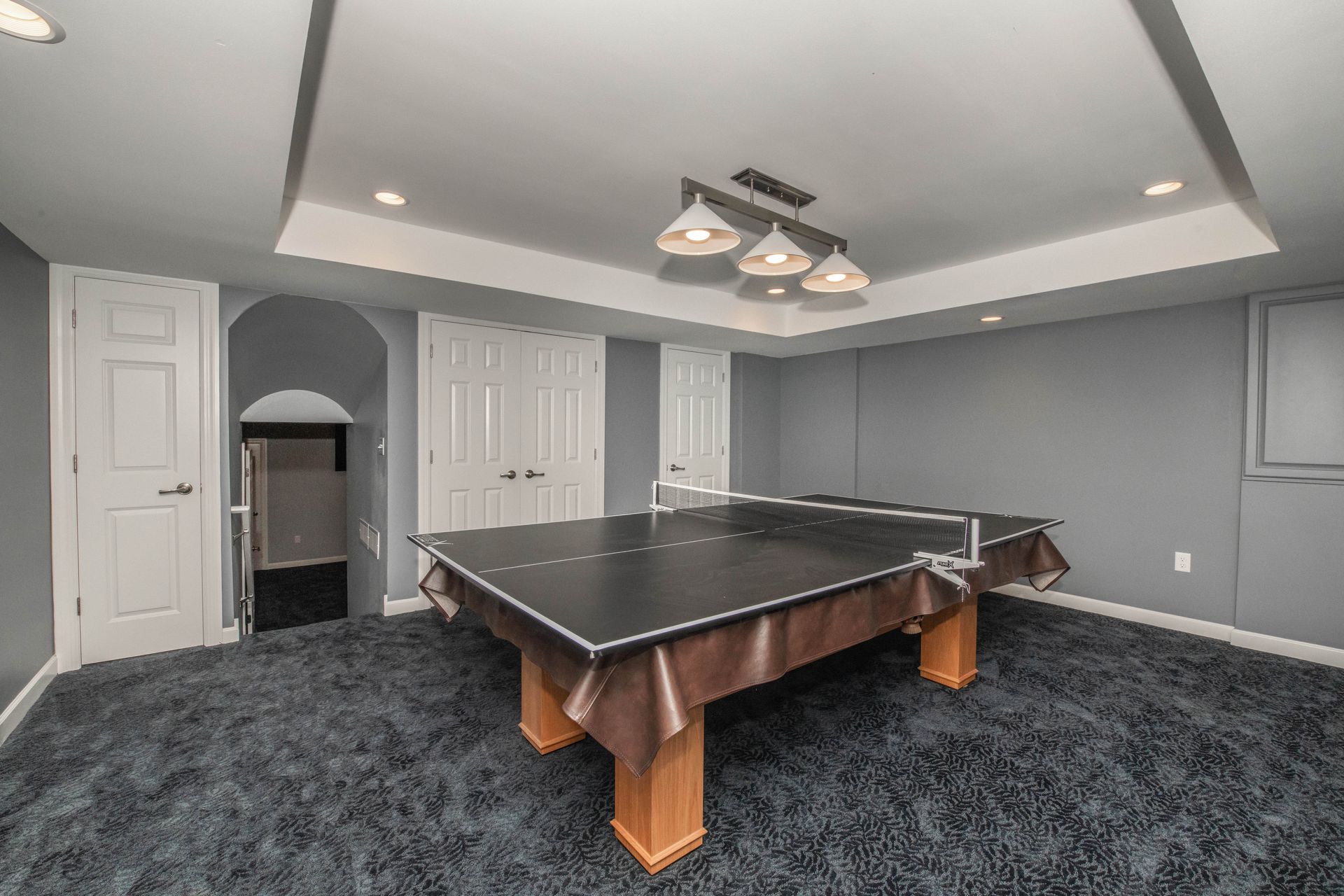 A ping pong table in a gray-walled finished basement with a dark blue carpet.