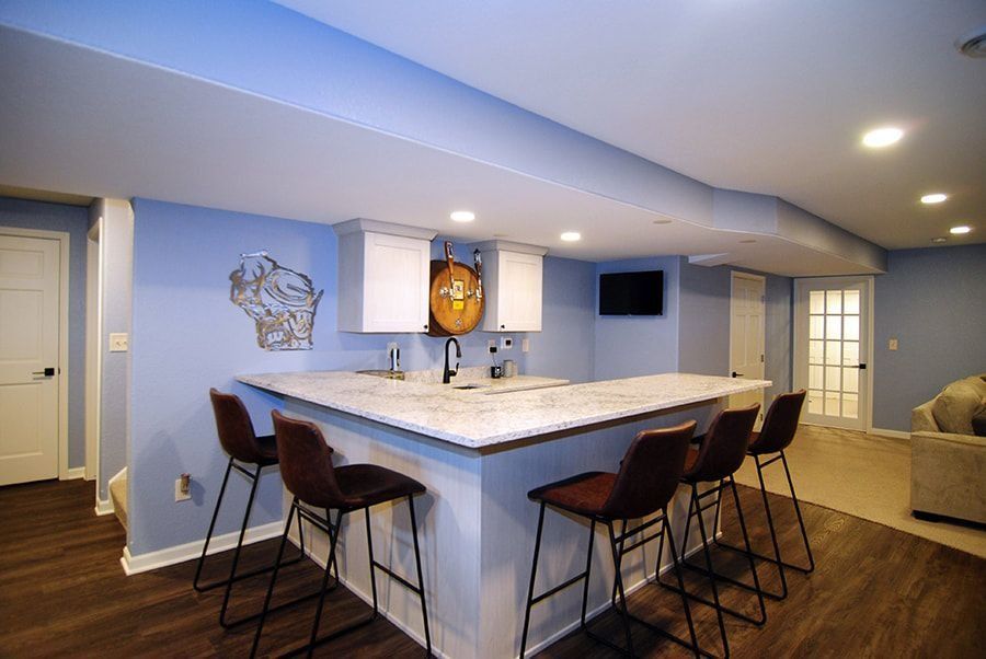 Basement bar with a countertop, stools, cabinets, a mounted TV, and a door. Blue walls, dark wood floor.
