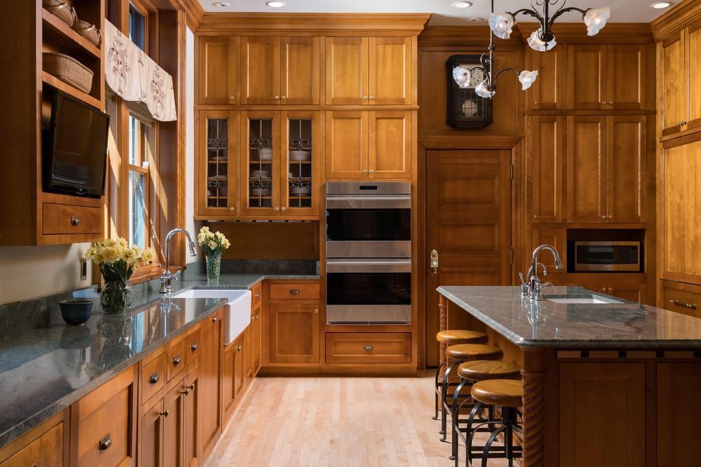 A spacious kitchen with natural wood cabinetry, a granite-topped island, stainless steel double ovens, and wood flooring.