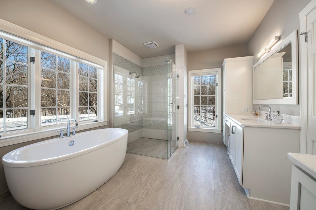 Spacious bathroom with a freestanding tub, glass shower, large windows, and white cabinetry.