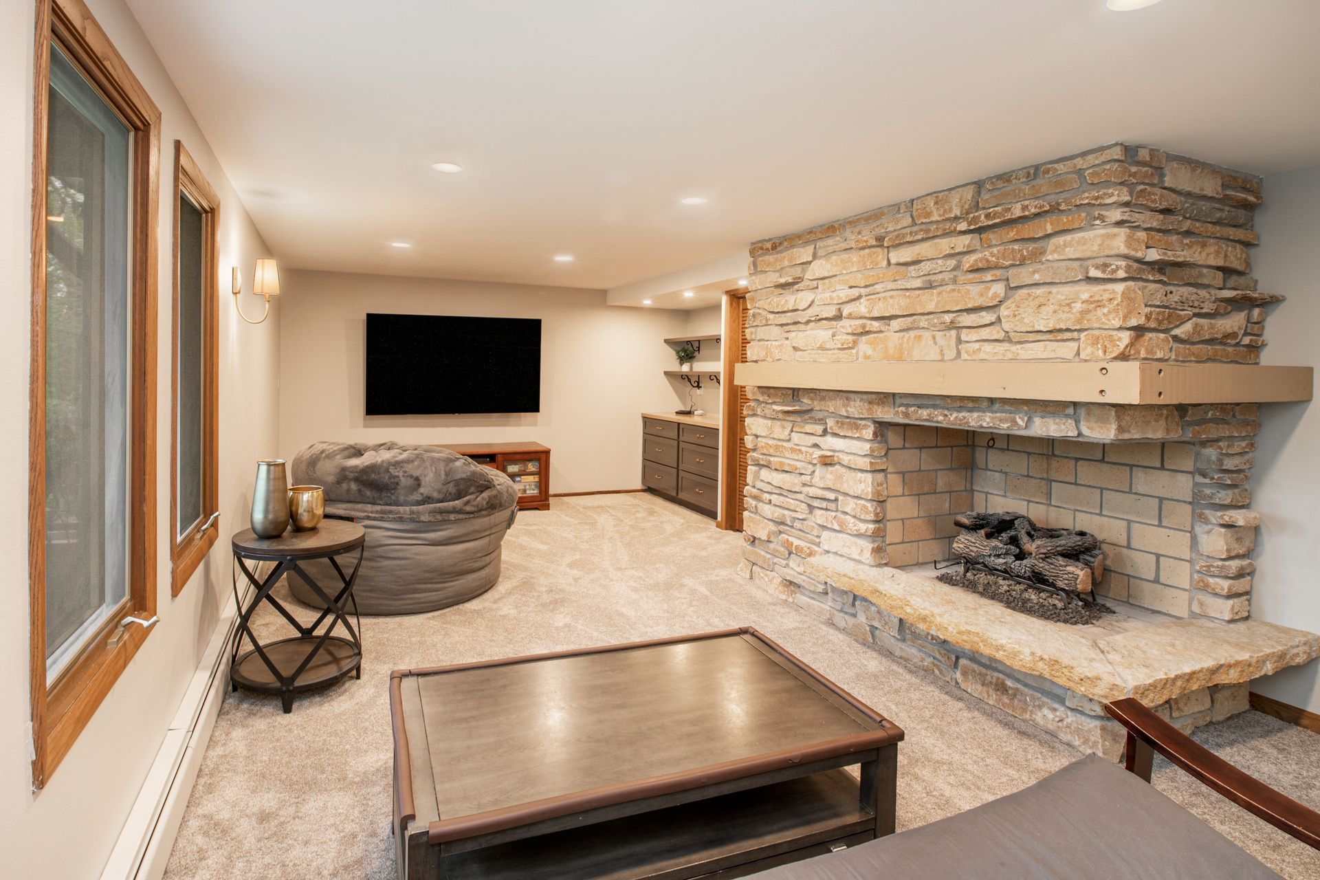 Cozy basement living room with stone fireplace, TV, and neutral-toned furniture.