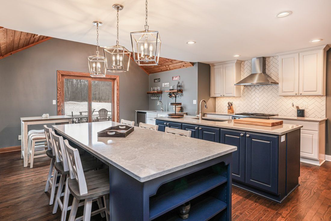 Spacious kitchen with a large blue island, white cabinets, and a light-colored countertop, with natural light and wooden floors.