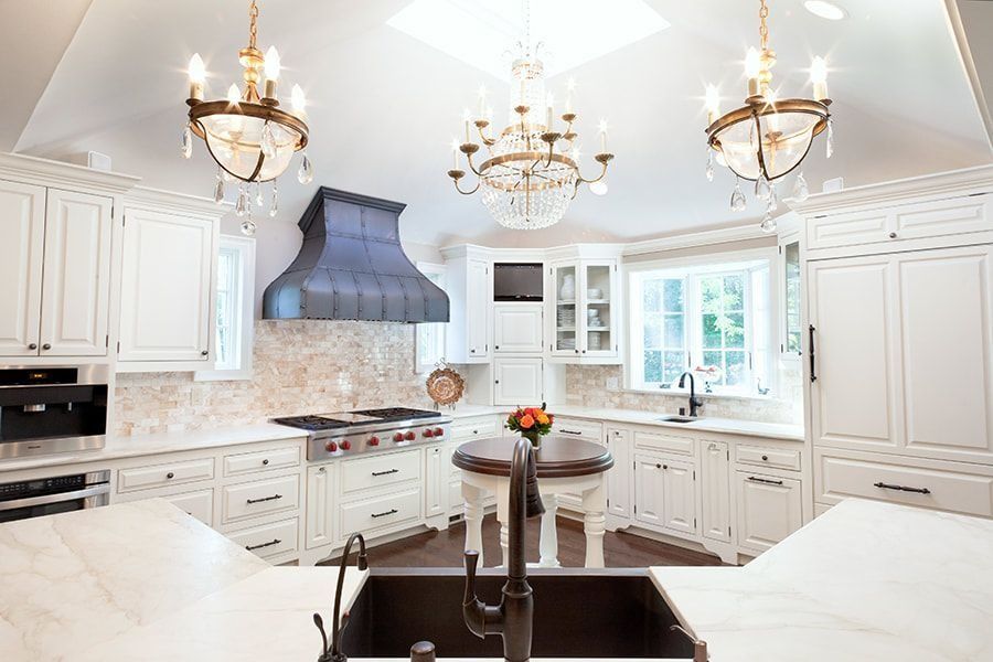 Elegant white kitchen with chandeliers, island, and a range hood.