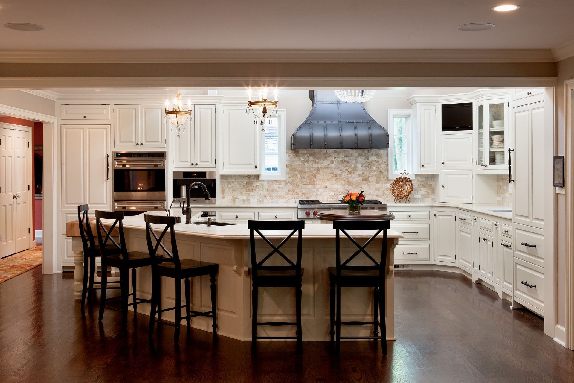 A bright kitchen with white cabinetry, a large center island with four dark chairs, and a dark range hood over the stove.