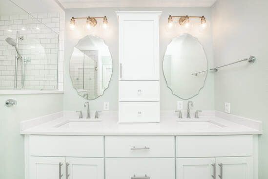 Bright white bathroom with dual sinks, oval mirrors, and overhead lighting.