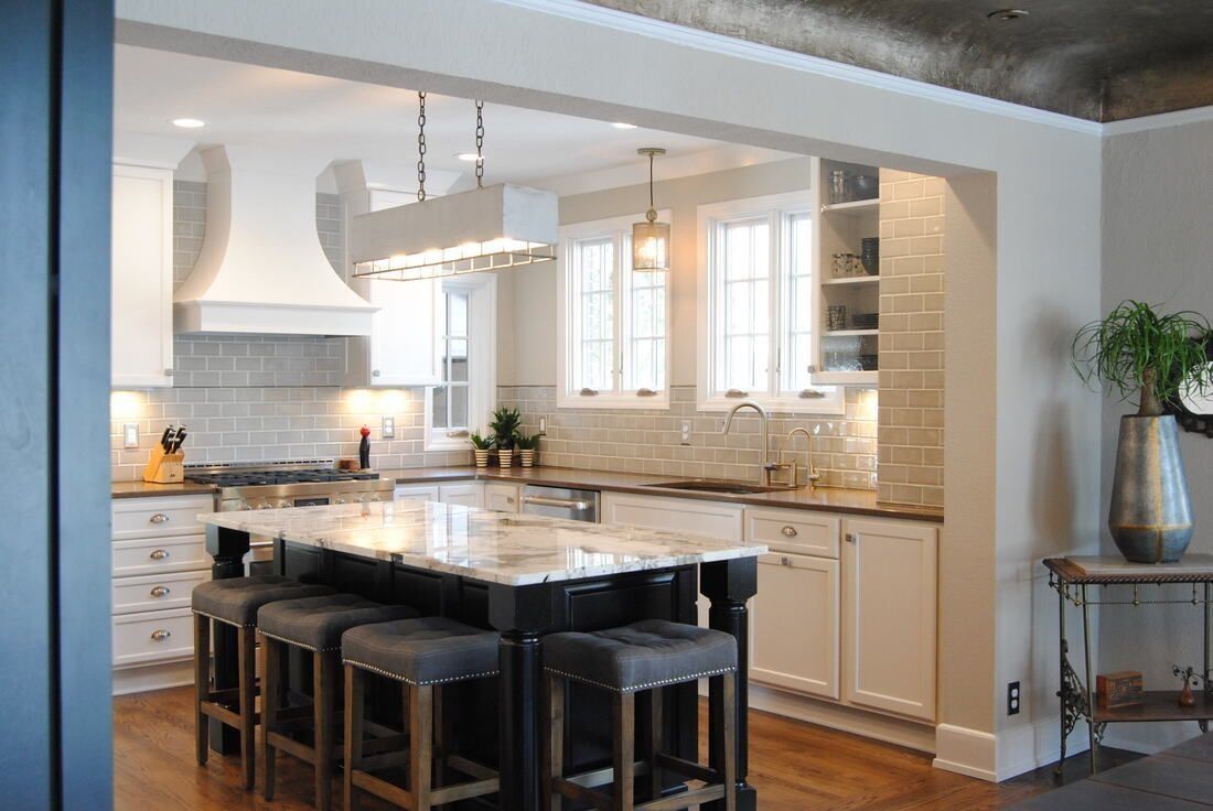 Kitchen with island, white cabinets, and gray tile backsplash. Bar stools, pendant lights, and windows.