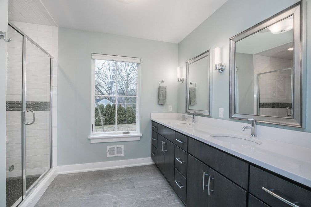 Modern bathroom with a double vanity, shower, and a window, painted light blue.