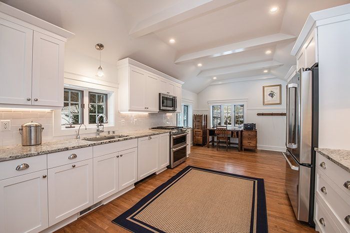 White kitchen with granite counters, stainless steel appliances, and hardwood floors; dining area in background.