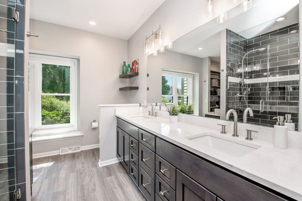 Bathroom with gray vanity, double sinks, large mirror, window, and glass shower.