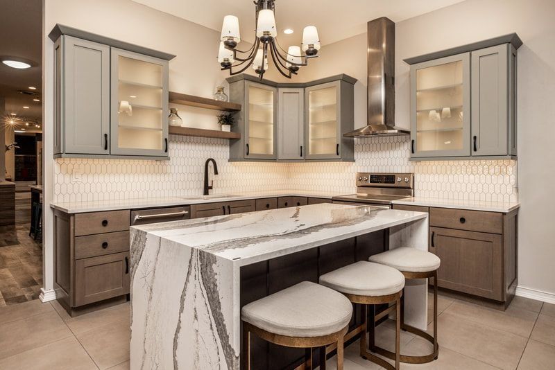 Modern kitchen with a marble island, gray cabinets, and three bar stools.