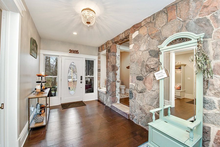 Entryway with stone wall, white door, wood floor, and a mint green mirror.