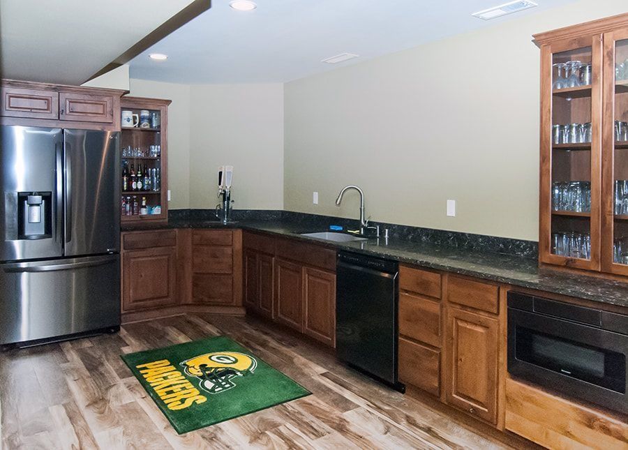 A basement bar with a fridge, cabinets, sink, and a Packers logo rug.