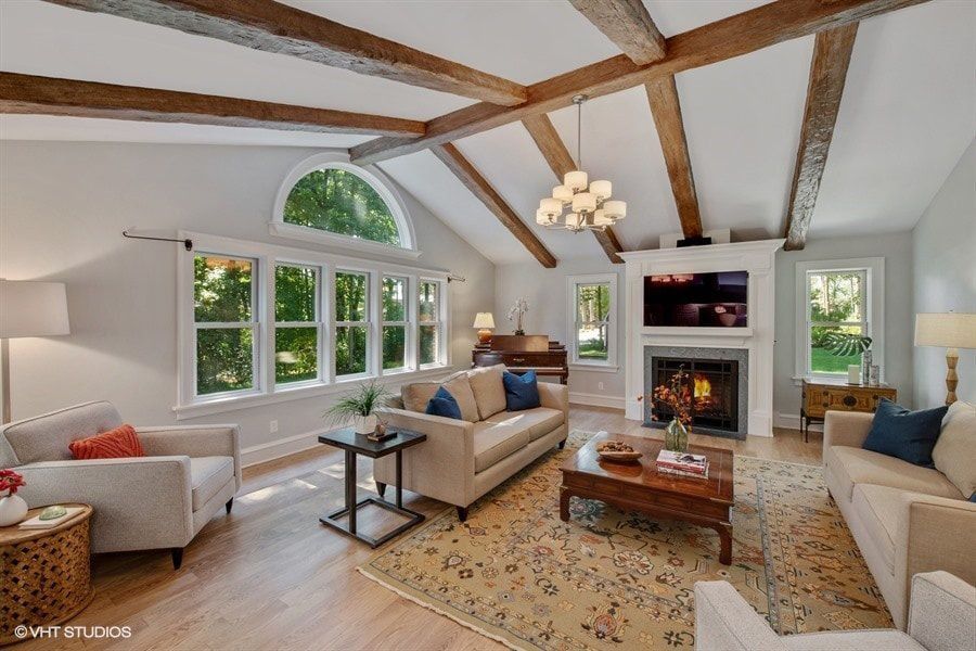 Living room with beige sofas, fireplace, wooden beams, and large windows.