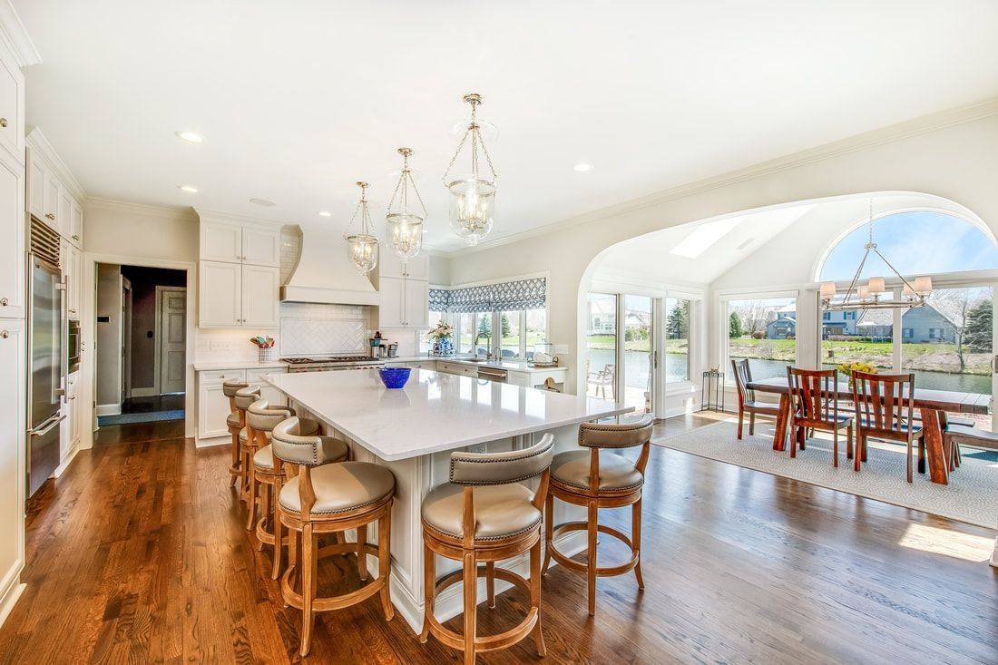 Bright, spacious kitchen with large island, stools, and dining area, overlooking a scenic outdoor view.