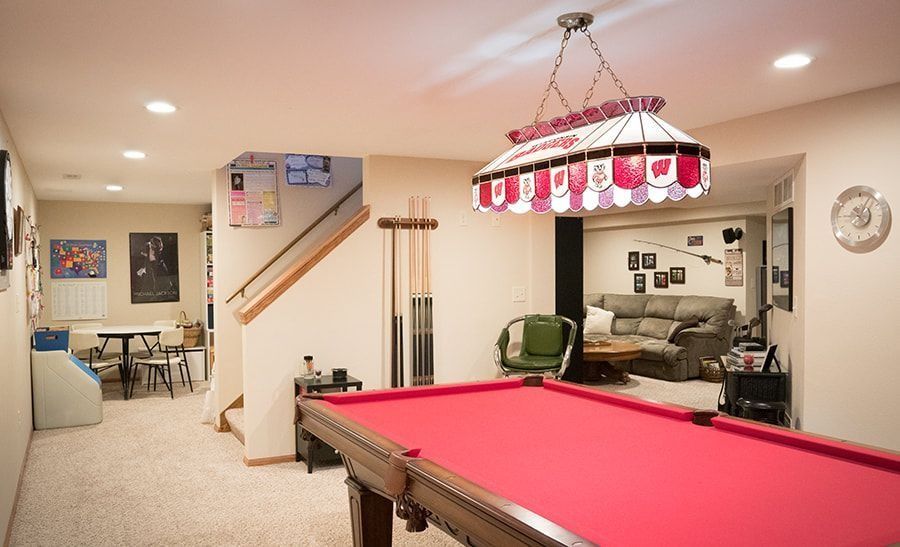 Pool table in a finished basement, red felt, Budweiser lamp, lounge area visible in the background.