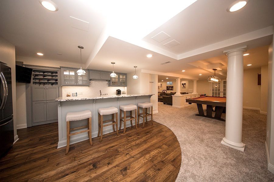 Basement entertainment area with a bar, seating, a pool table, and wood flooring.