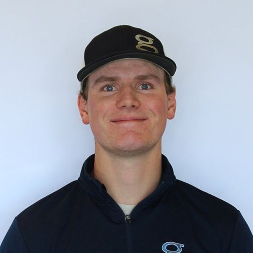 Smiling young man in a navy jacket and black baseball cap with a gold 