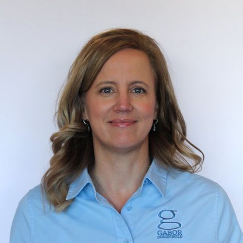 Denise with blonde hair wearing a light blue shirt with the Gabor logo, smiling in front of a white wall.