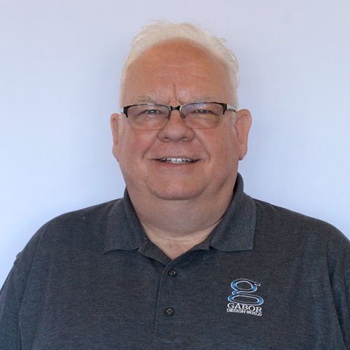 Michael-John with glasses smiles, wearing a gray polo shirt. Studio headshot.