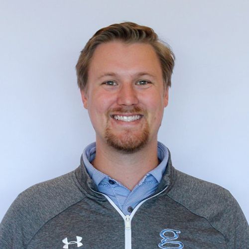 Ryan in a blue shirt and gray jacket; light hair and stubble; plain white background.