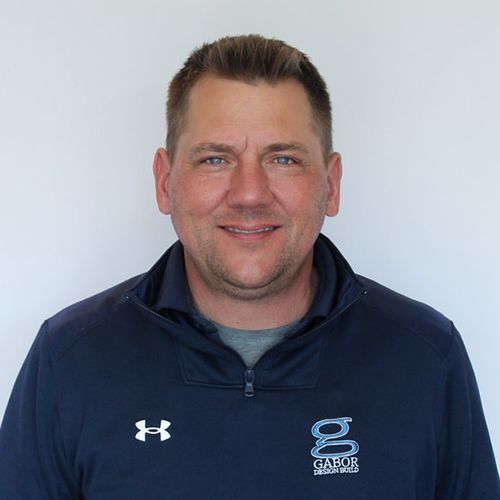 Man in a navy blue athletic jacket with a gray shirt underneath, smiling.  White background.
