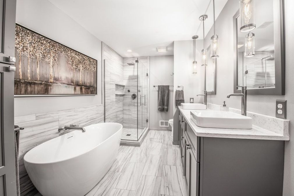 Modern bathroom with a bathtub, shower, double vanity, and artwork; white and gray color scheme.