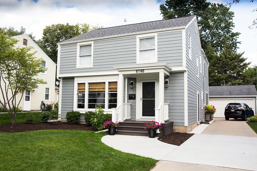 Two-story house with gray siding, white trim, and a small porch; car parked in the driveway.