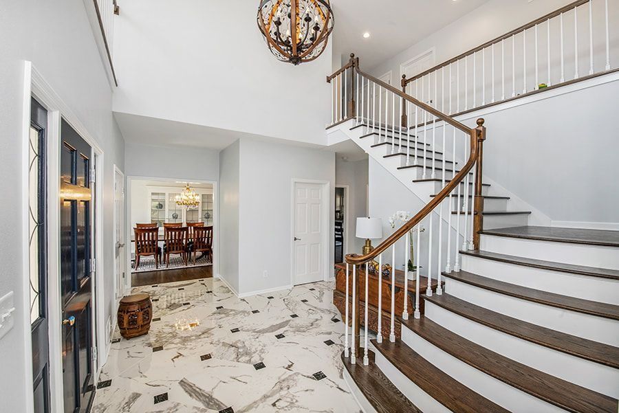A grand foyer with a staircase, marble floors, and an ornate chandelier.