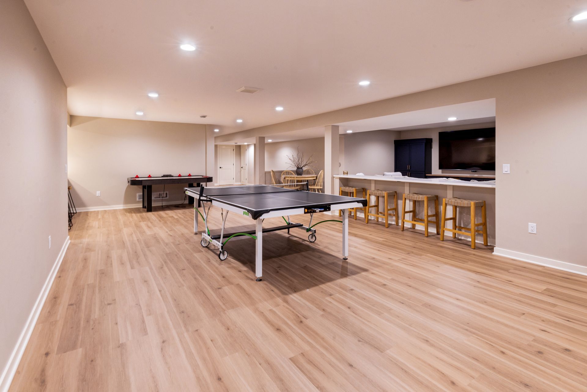 Spacious finished basement with ping pong table, bar, and light wood flooring.