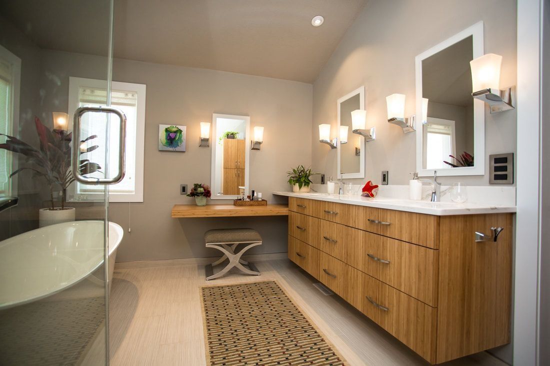 Modern bathroom with light wood vanity, dual sinks, large mirrors, and a freestanding tub.