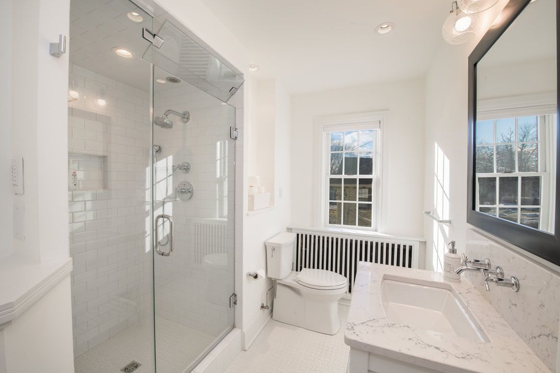 White bathroom with glass shower, toilet, sink, window, and mirror.