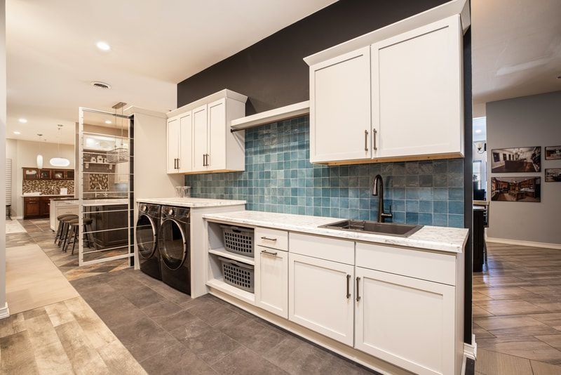Laundry room with white cabinets, black appliances, blue tile backsplash, and a dark gray floor.