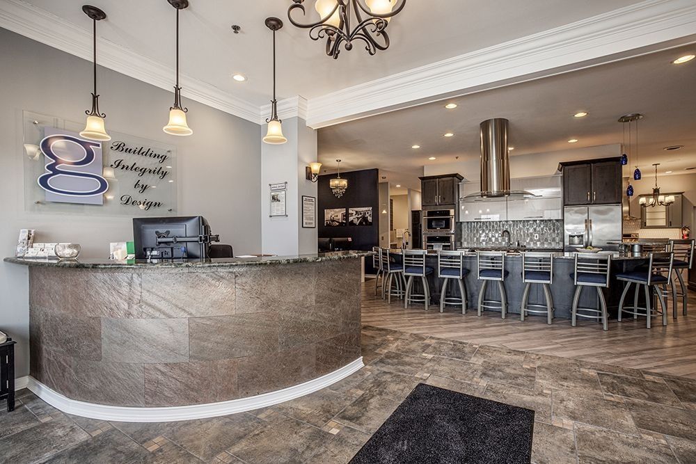 Reception area with kitchen display: brown counter, gray walls, black stools, and modern appliances.