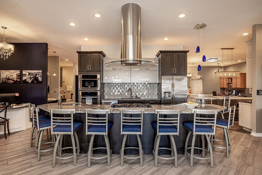 Spacious kitchen with island seating, stainless steel appliances, dark cabinetry, and blue barstools.