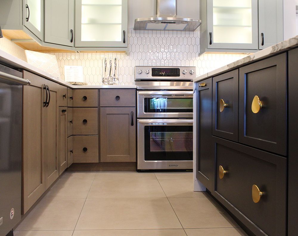 Modern kitchen with gray, tan, and black cabinets, stainless steel appliances, and gold knobs.