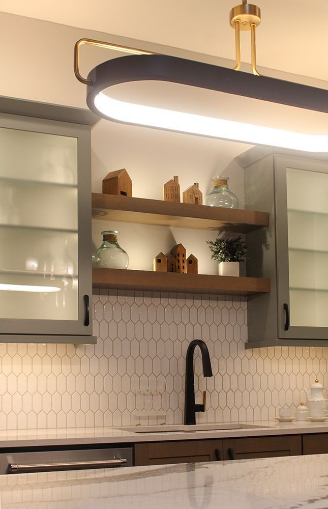 Kitchen with wooden shelves displaying miniature houses and plants, above a sink with a black faucet, white tile backsplash.