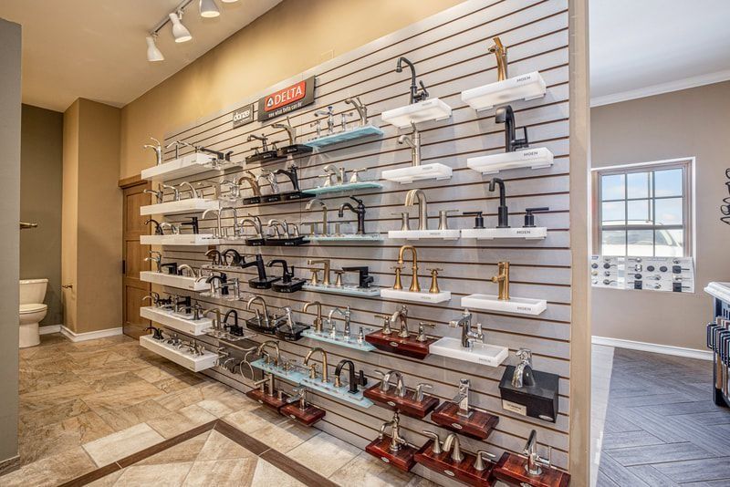 Showroom display of various bathroom faucets on a slat wall with shelving, showcasing different styles and finishes.