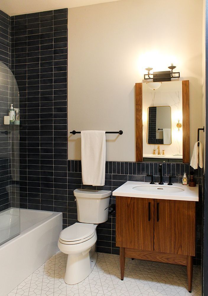 A bathroom with a dark tiled wall, wooden vanity, toilet, and white towel.