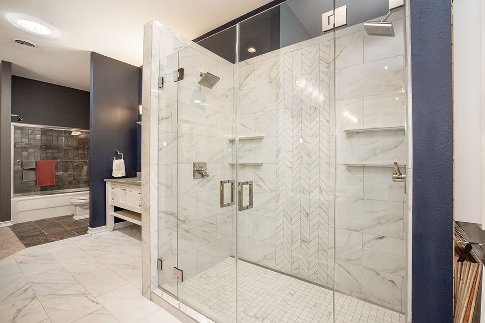 Spacious bathroom with marble shower, glass doors, and white floor tiles; blue walls.