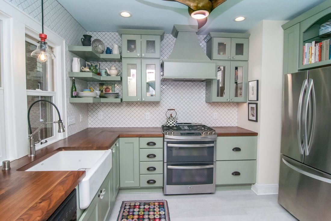 A mint green kitchen with wood counters, stainless steel appliances, and white patterned backsplash.