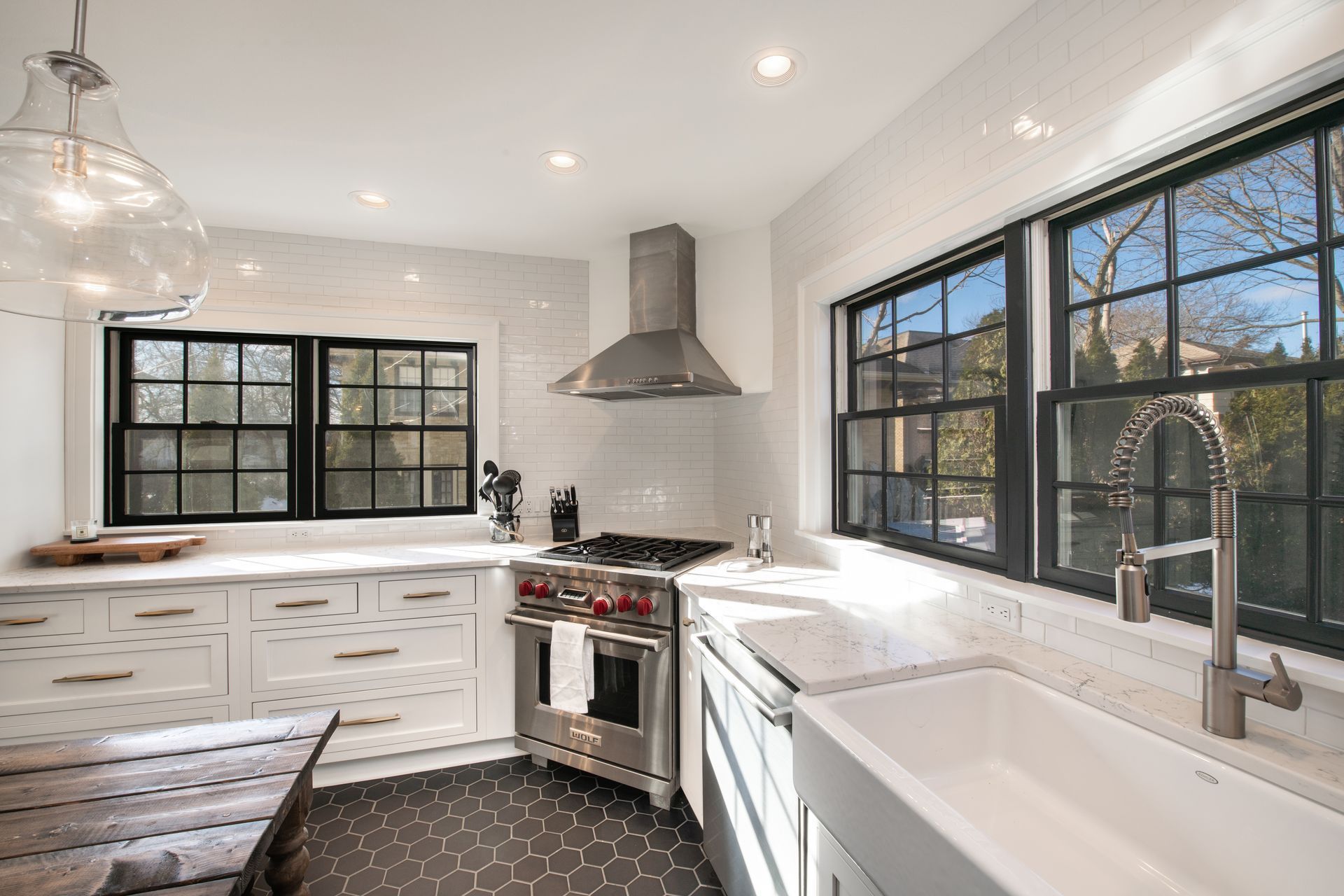A bright kitchen features white cabinets, a farmhouse sink, stainless steel appliances, and a geometric tiled floor.