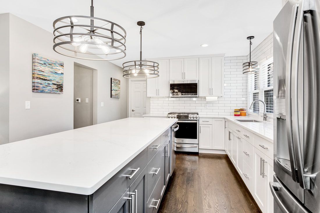Modern kitchen with white cabinets, gray island, stainless steel appliances, and pendant lights.