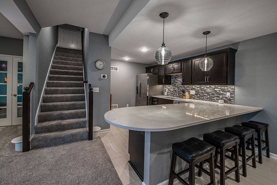 Kitchen with gray walls, dark cabinets, and a curved island with bar stools; stairs to the left.