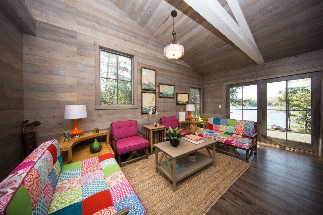 Cozy living room with wood walls, patchwork furniture, a jute rug, and a view of a lake.
