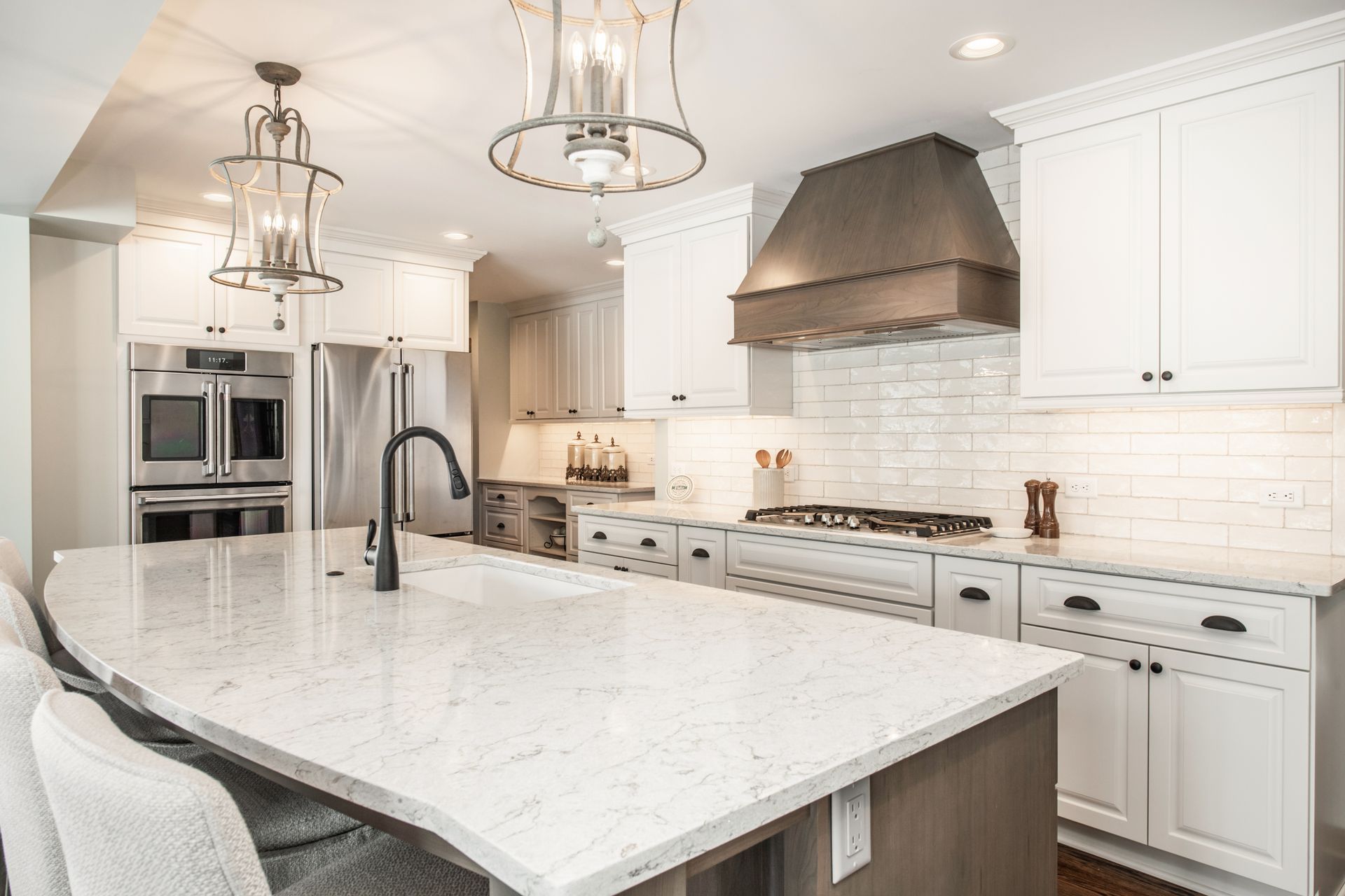 Modern kitchen featuring a large white marble island, white cabinetry, stainless steel appliances, and two pendants.
