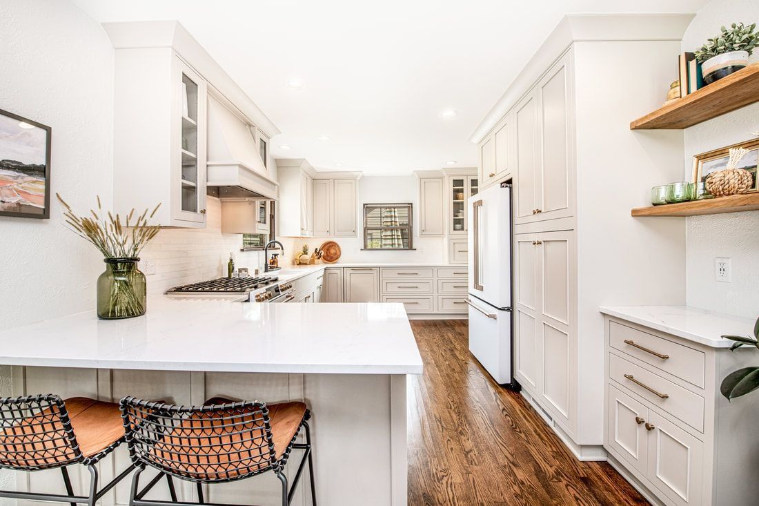 Bright, modern kitchen with white cabinets, wooden floor, and a white countertop island with bar stools.