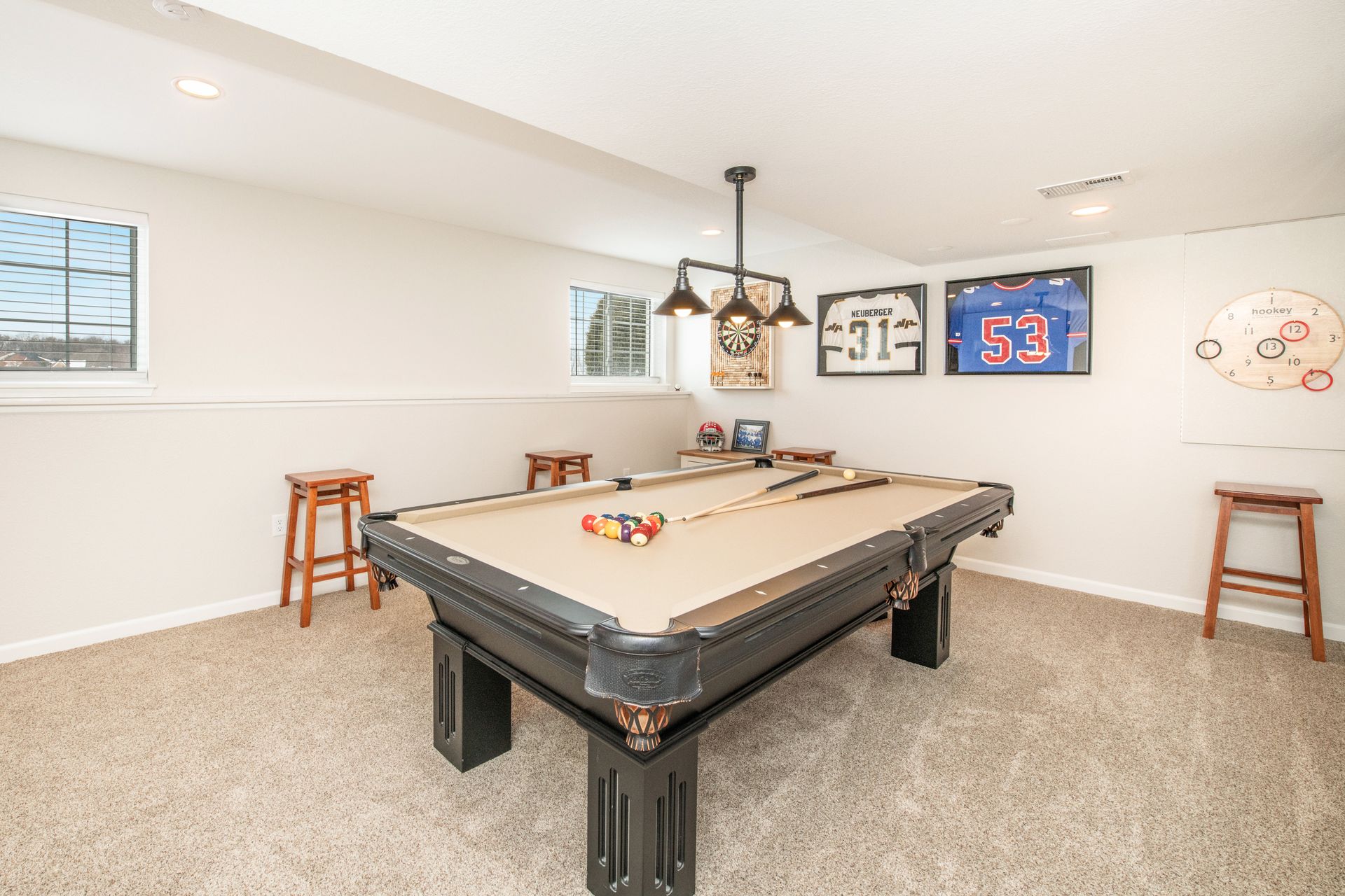 Pool table in a game room with sports memorabilia on the wall and two bar stools.