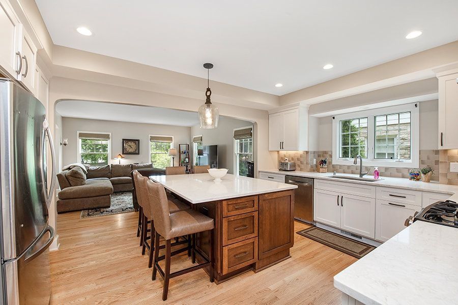 Spacious kitchen with island, light cabinets, and hardwood floors, opens to a living room with a sectional sofa.