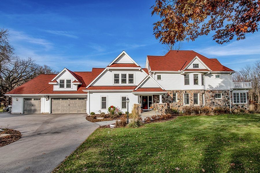 White house with red roof, stone accents, and a green lawn under a blue sky.
