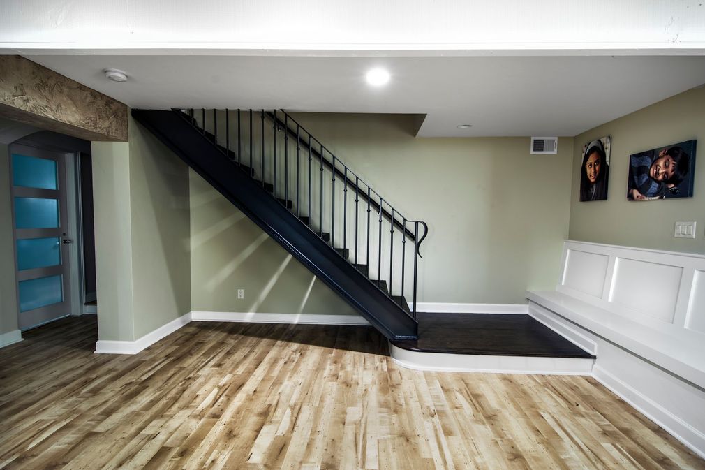 A black metal staircase in a room with light wood floors, sage green walls, and white built-in bench seating.